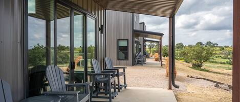 Un espacio de estar al aire libre techado con sillas y mesas, con vista a un paisaje natural.