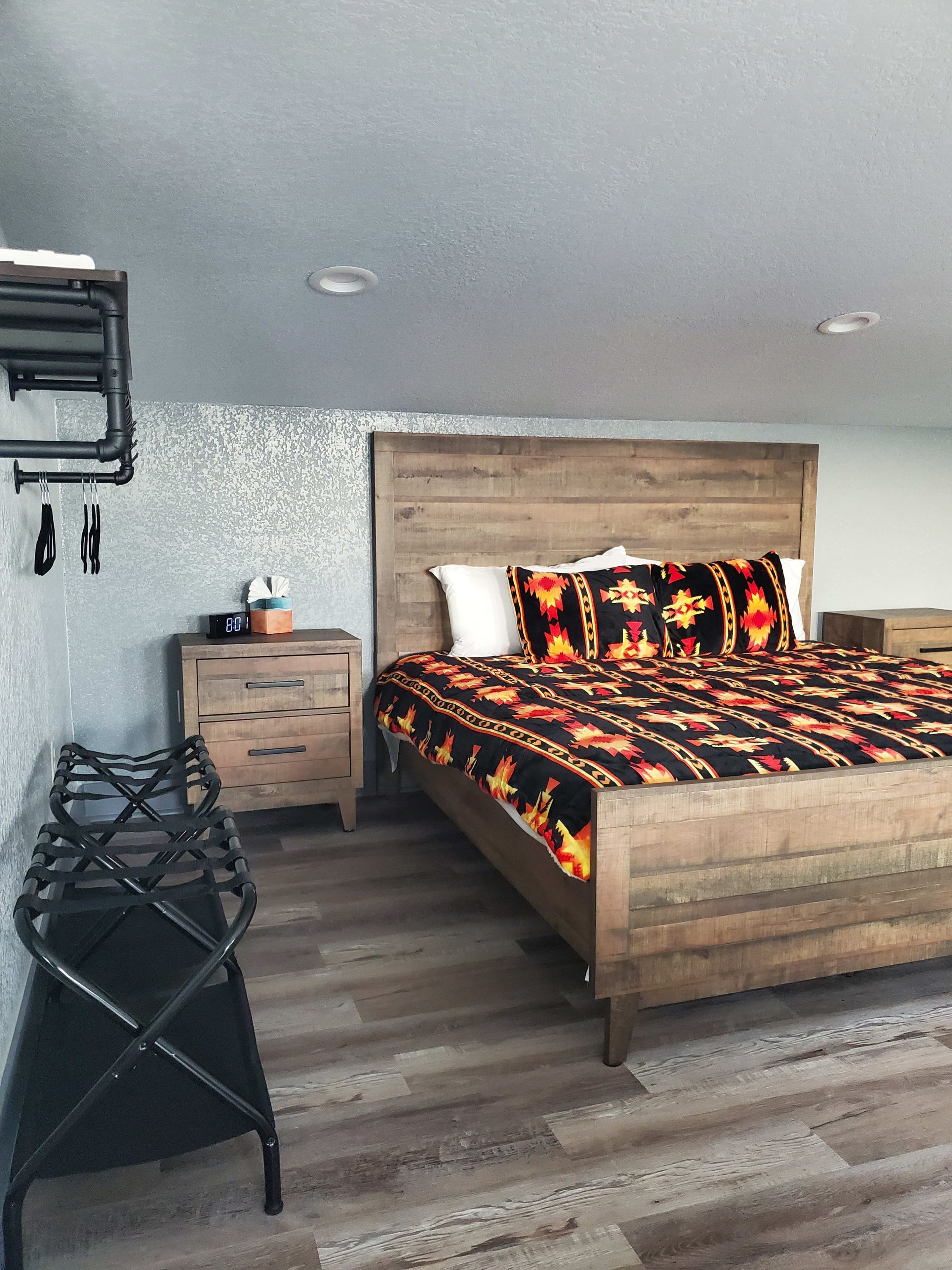 A bedroom with a wooden bed, a nightstand, a chair, and a wall-mounted shelf with utensils.