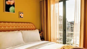 Ein Hotelzimmer mit Bett, Blick auf die Stadt durch ein großes Fenster und einer Wand mit zwei gerahmten Bildern.