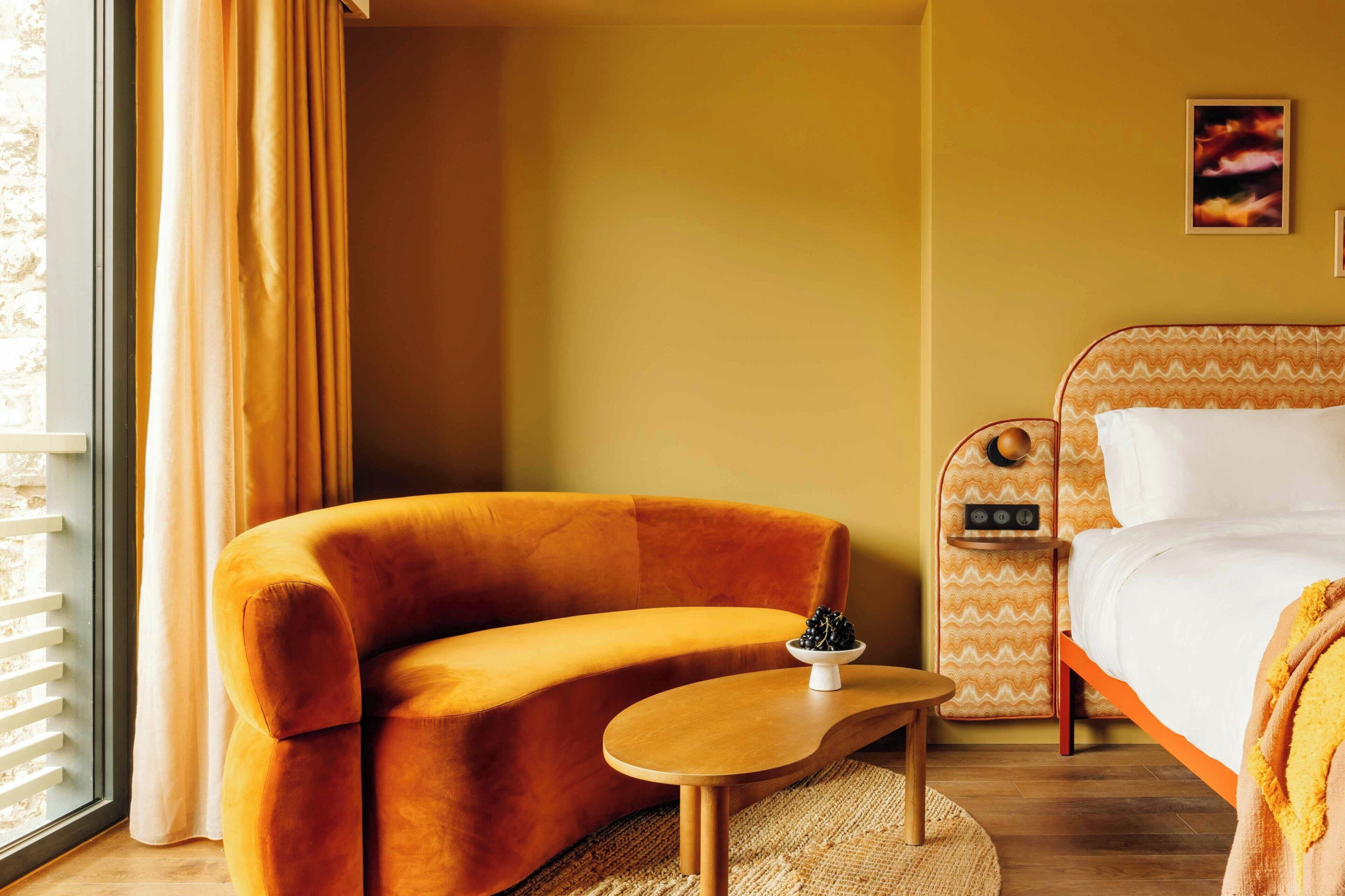 A room with a sofa, a small table, a bed, and a window with curtains.