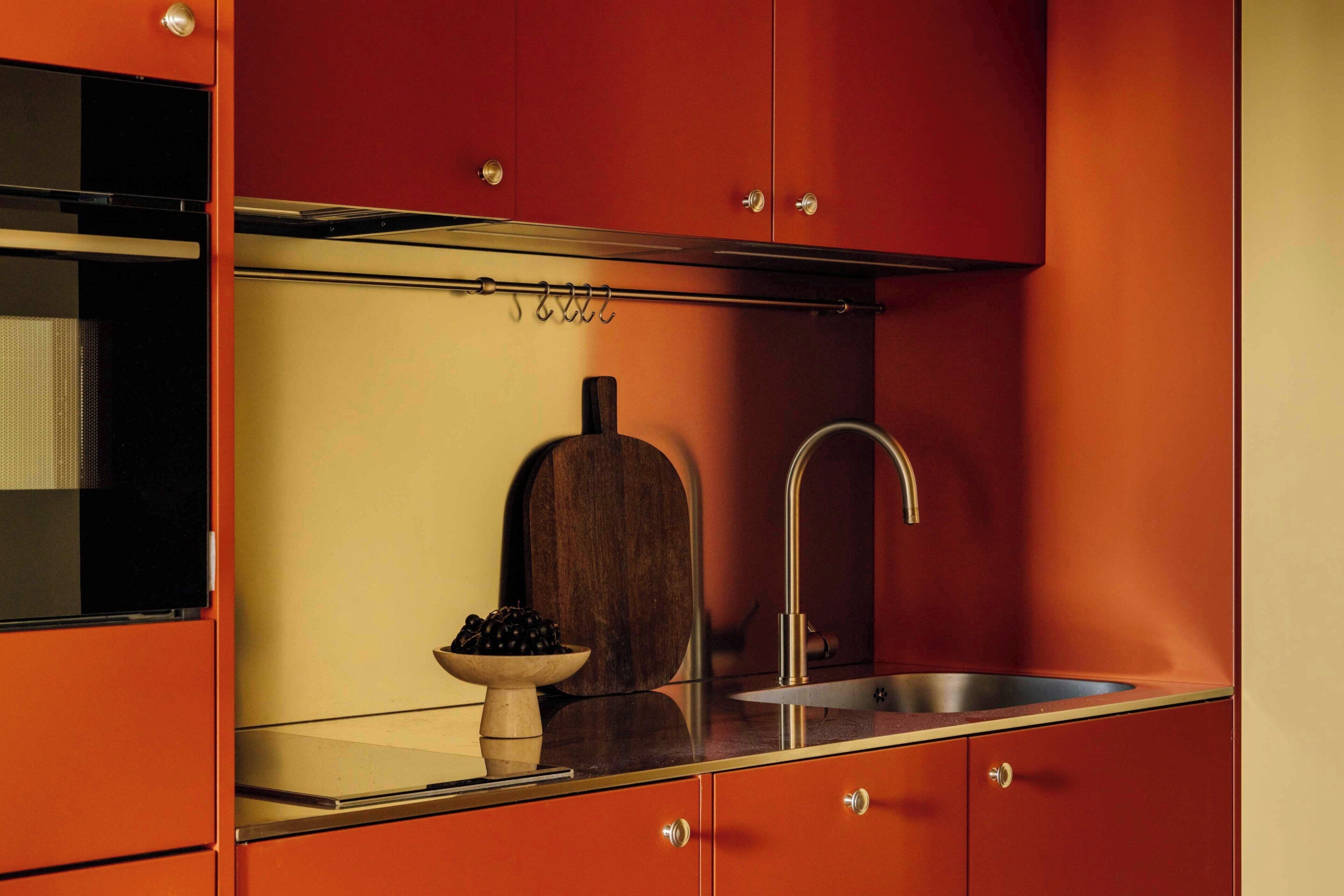 A kitchen with a sink, a wooden cutting board, and a bowl of fruit.