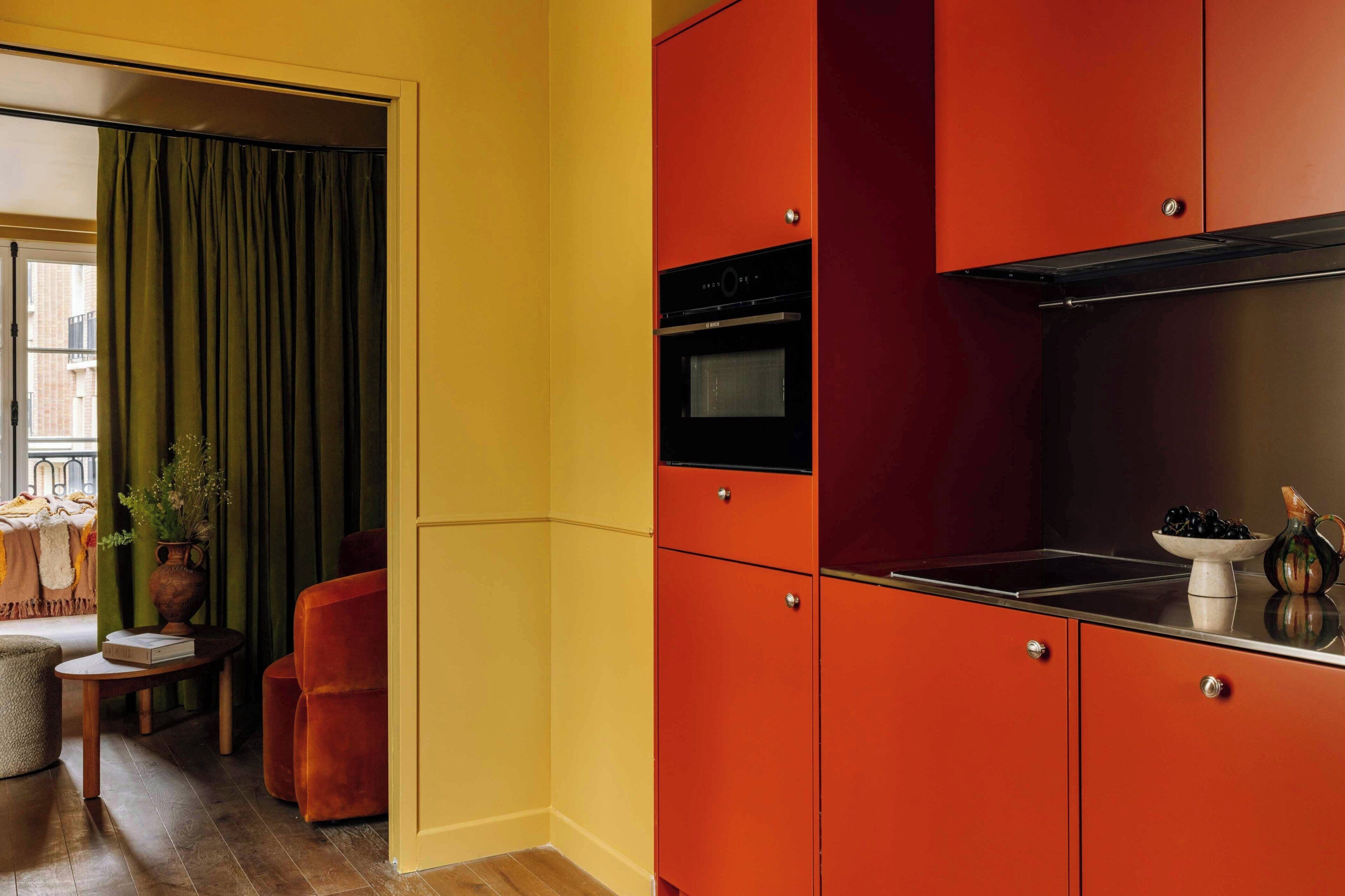 A kitchen with red cabinets, a black oven, and a window with curtains.