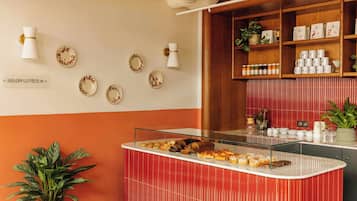 A reception area with a counter displaying pastries, a wall with decorative plates, and a shelf with kitchen items.