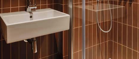 Un baño con lavamanos blanco, ducha y paredes de azulejos marrones.