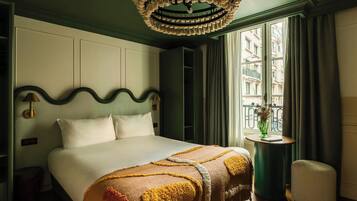 Een hotelkamer met een groot bed, een ronde tafel met een vaas en uitzicht op gebouwen door het raam.