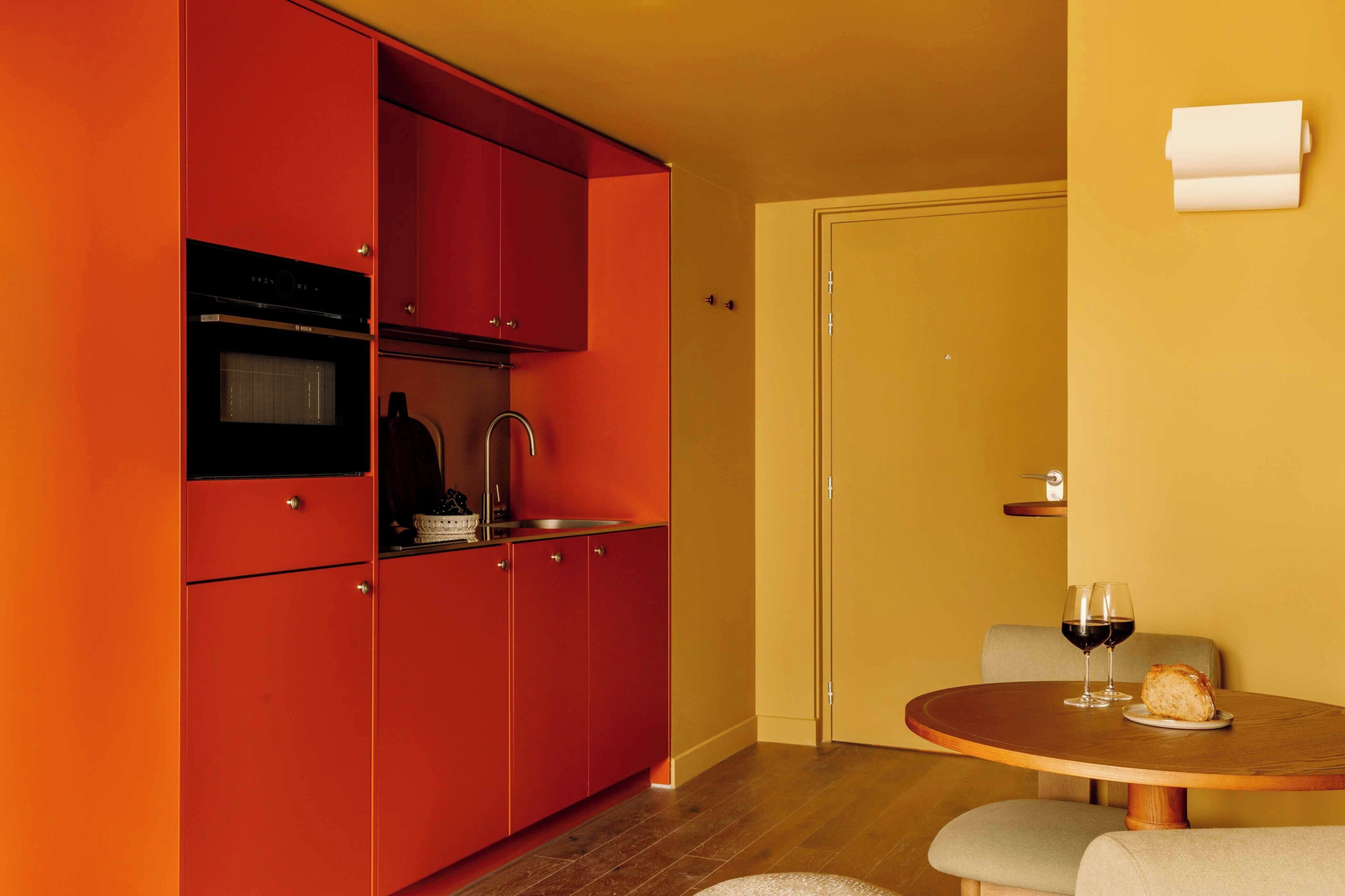 A compact kitchen with red cabinets, a sink, and a dining area with a round table and two chairs.