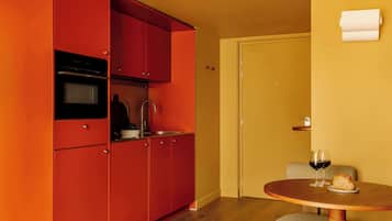 A compact kitchen with red cabinets, a sink, and a dining area with a round table and two chairs.