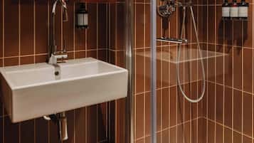 Une salle de bain avec un lavabo blanc, une douche équipée d’un pommeau de douche à main et un espace de douche fermé par des parois en verre.