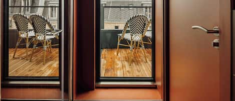 A room with a sliding glass door leading to a balcony with two wicker chairs and a wooden floor.