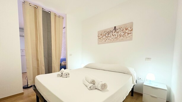 Un lit bien fait, avec des serviettes pliées, une table de chevet avec une lampe et un tableau accroché au mur.