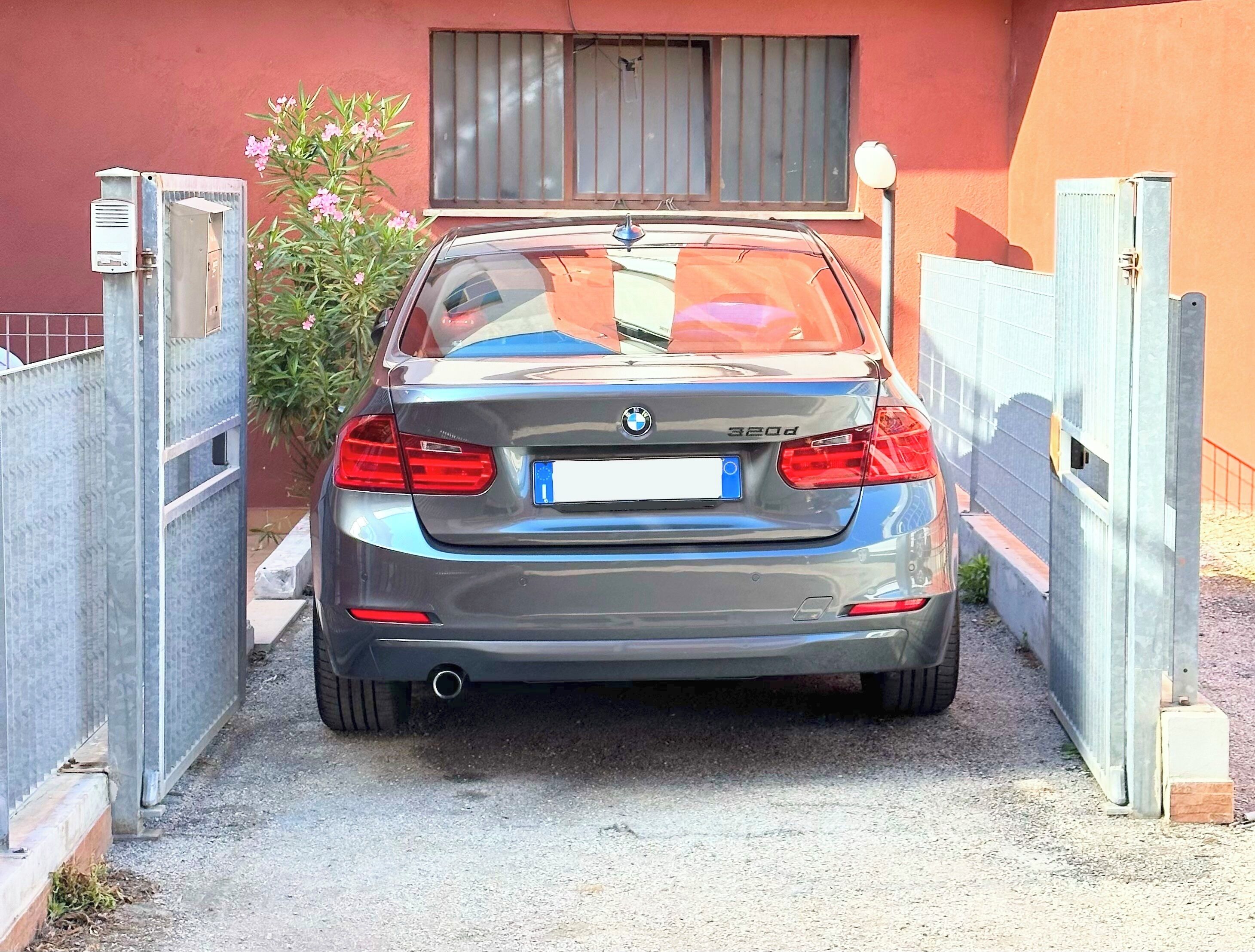 Ein BMW 320d vor einem verschlossenen Eingangsbereich mit roter Mauer und einem Fenster darüber.