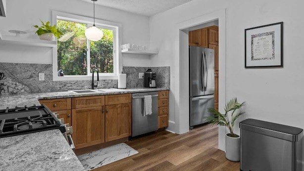 A modern kitchen with wooden cabinets, a stainless steel refrigerator, a built-in oven, and a window with a view of greenery.