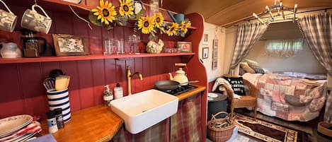 A cozy, compact room with a wooden bar area, a white sink, and a bed with a plaid blanket.