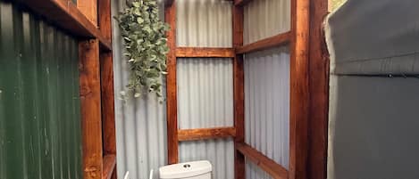 A small, enclosed bathroom with a wooden ceiling, a toilet, and a trash bin.
