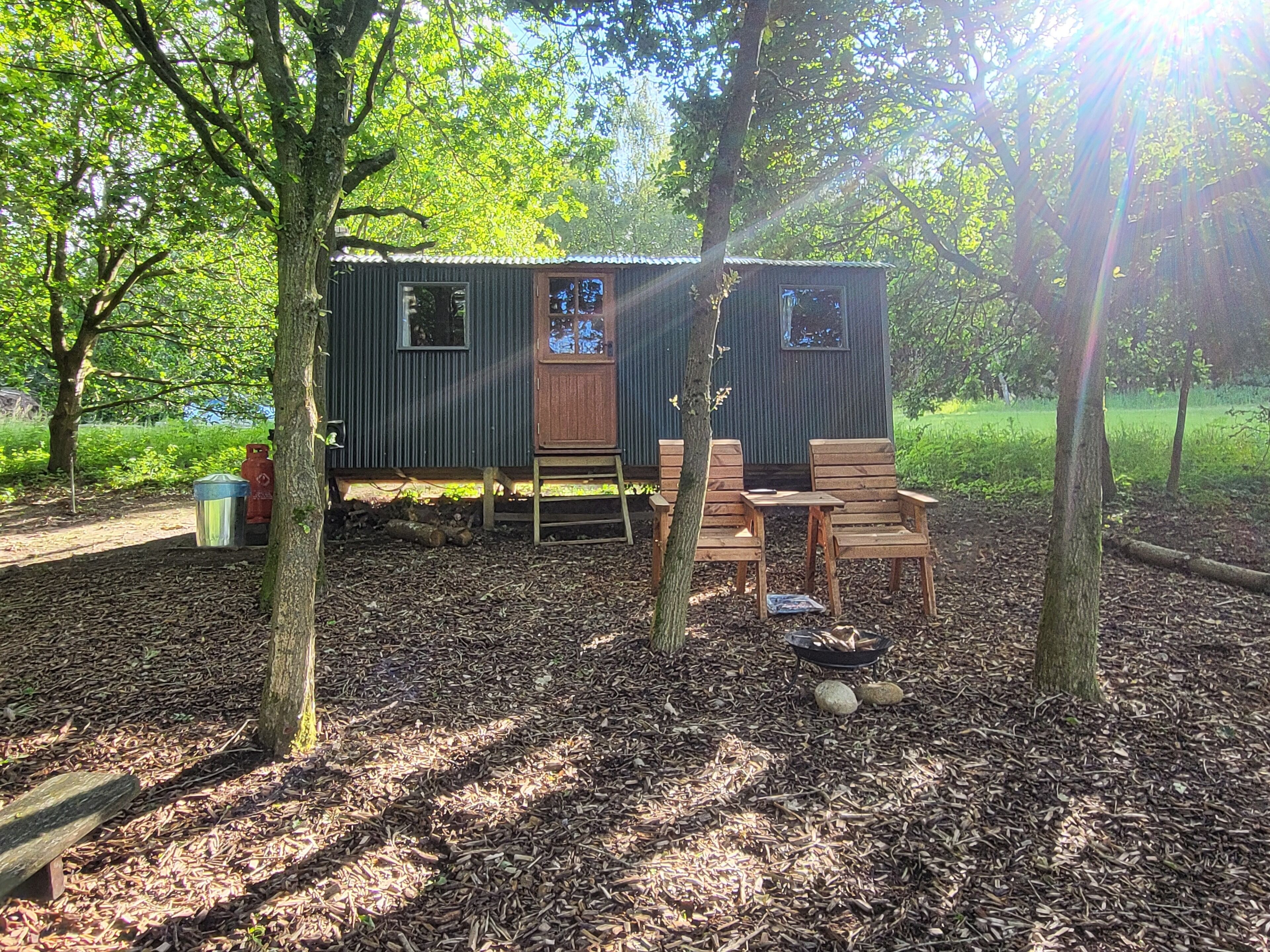 A small cabin with a wooden deck, a fire pit, and a door with a window.