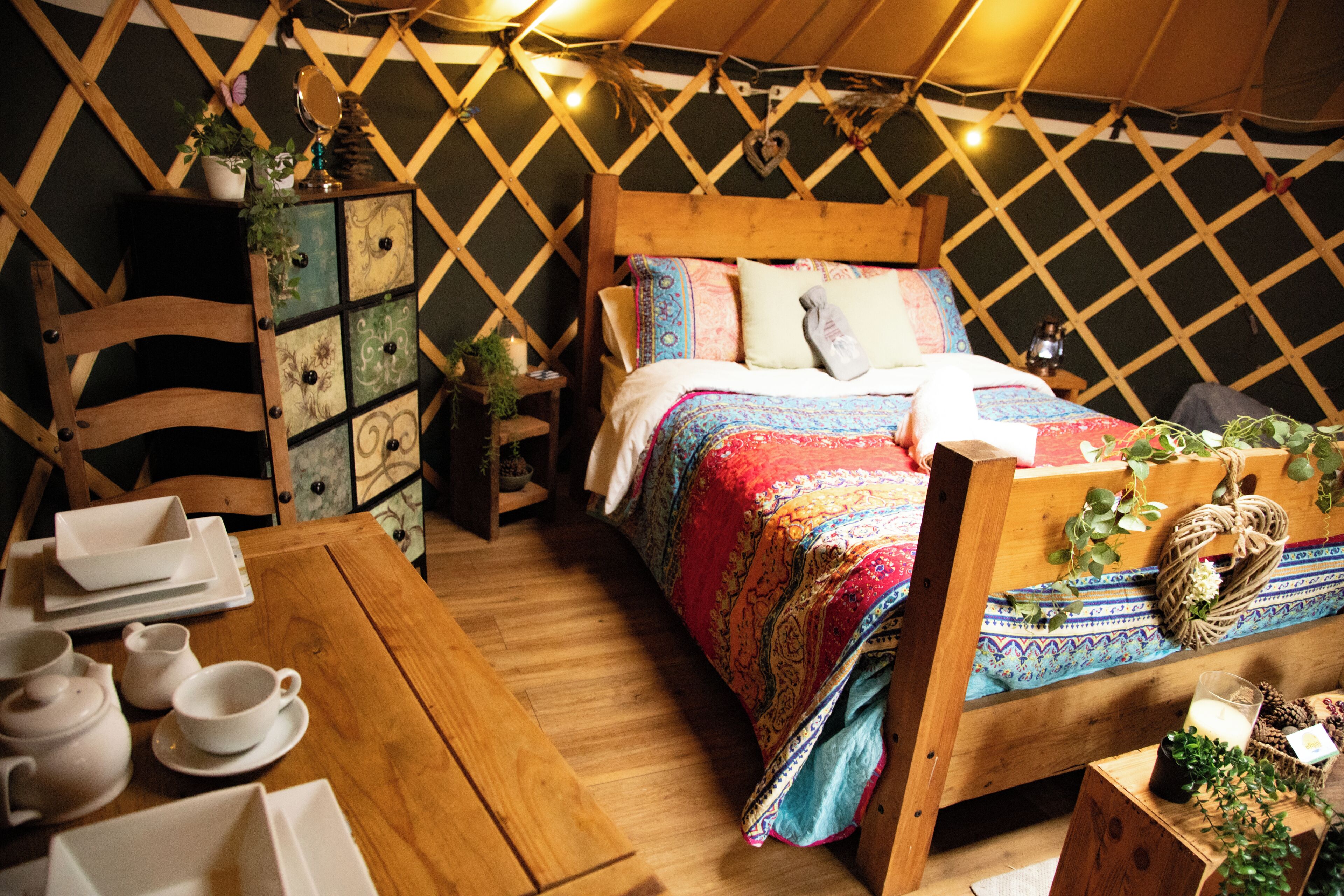 Una tienda acogedora y bien iluminada con una cama de madera, una mesa con juego de té y un aparador decorativo.