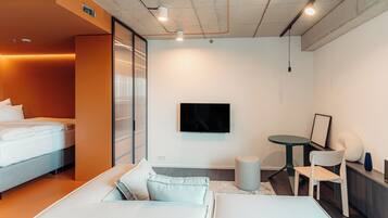A modern hotel room with a bed, a sofa, a small table, and a TV mounted on the wall.