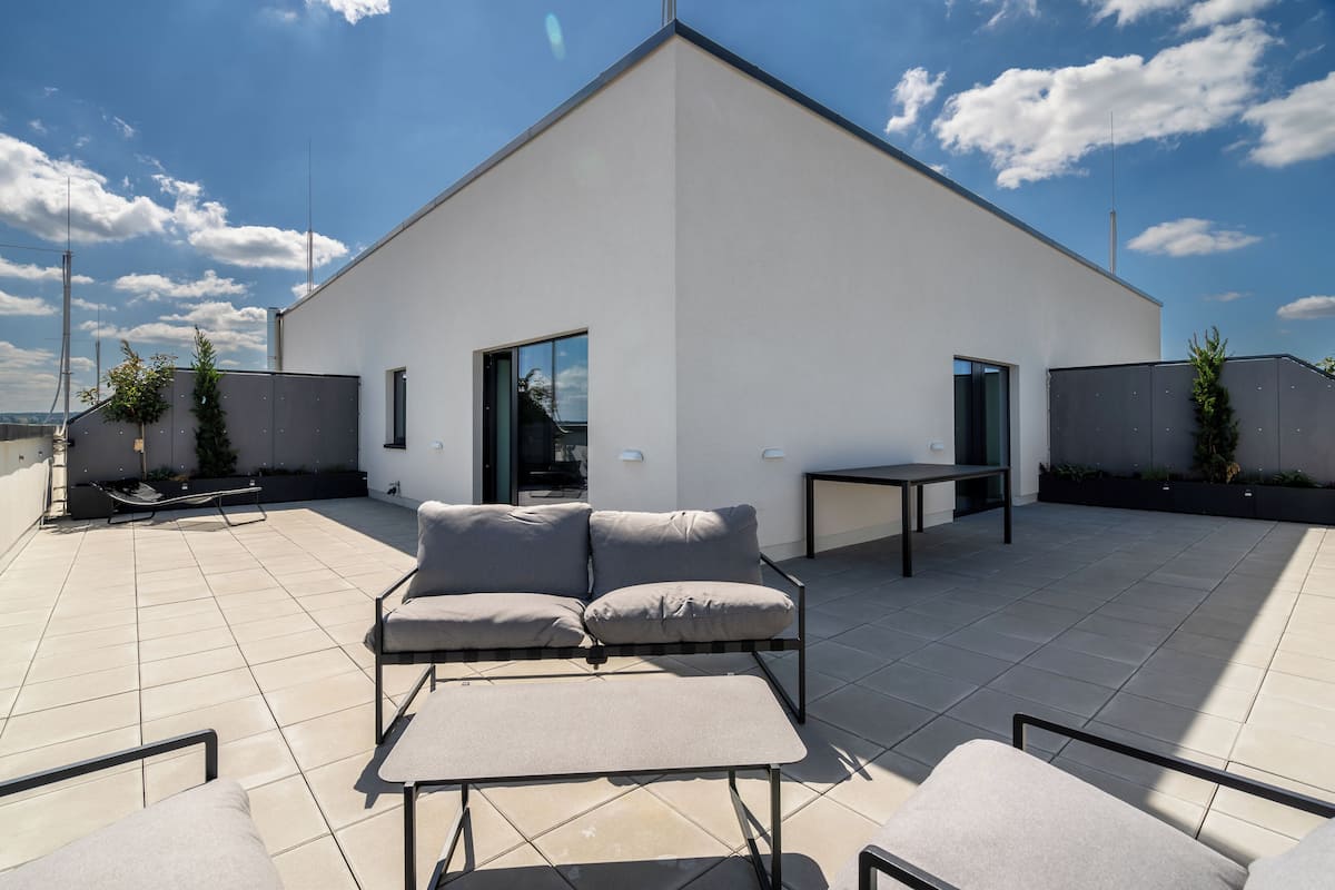A modern rooftop patio with a minimalist design, featuring a sofa, a small table, and potted plants.