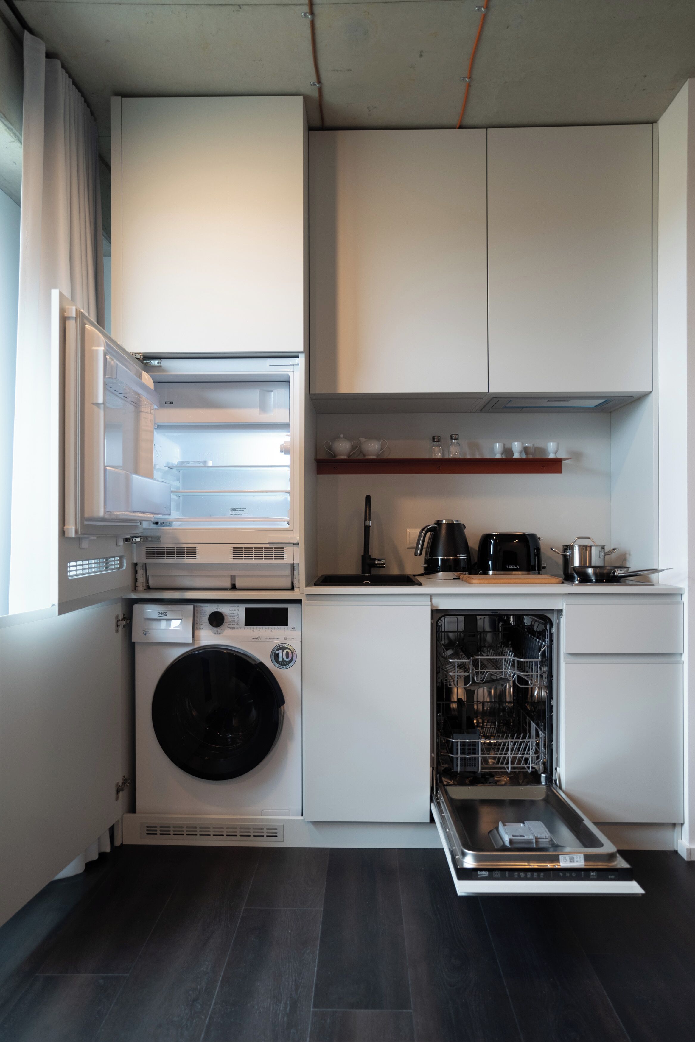 A compact kitchen with a built-in washer and dryer, a dishwasher, and a coffee maker on the countertop.
