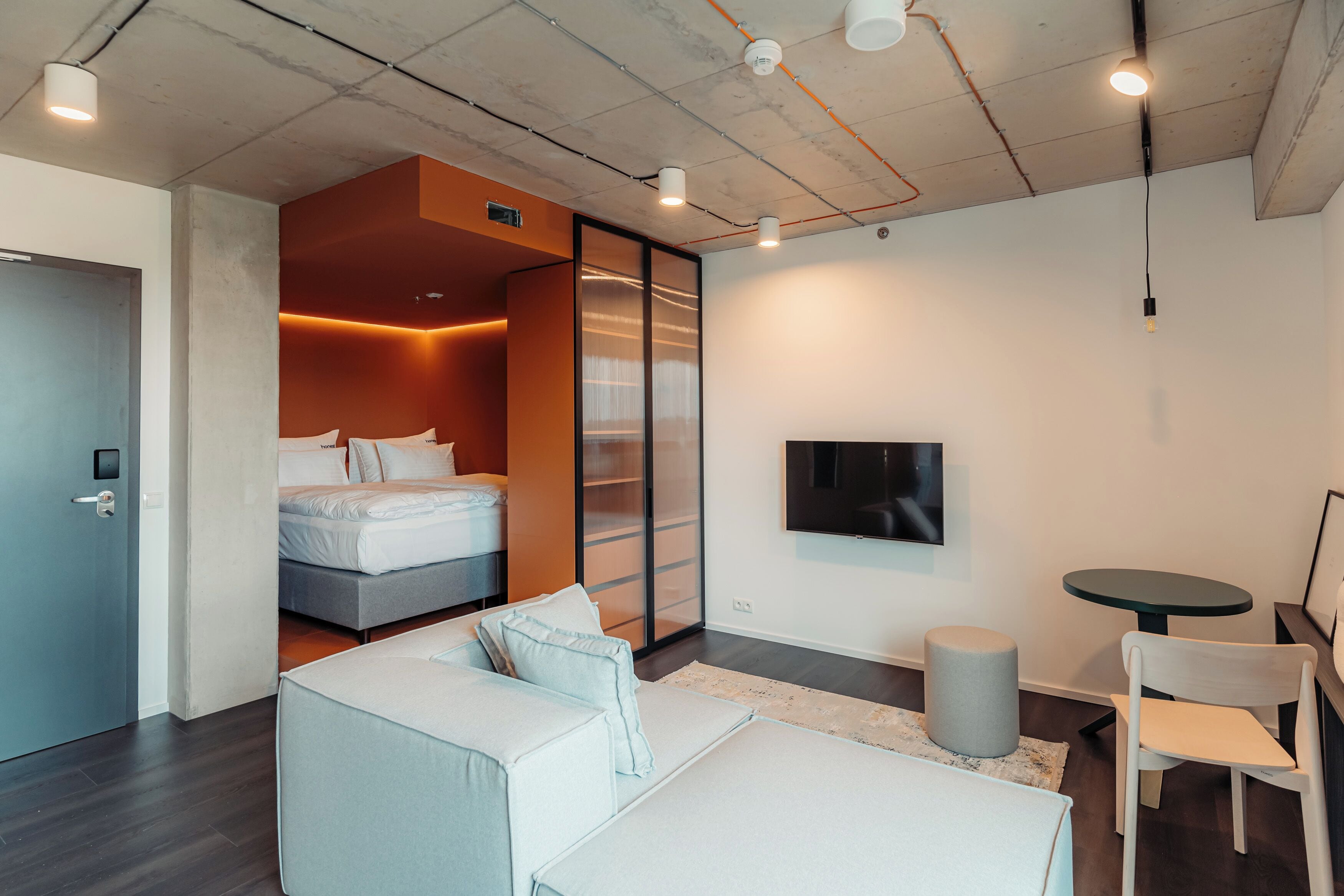 A modern hotel room with a bed, a sofa, a small table, and a TV.