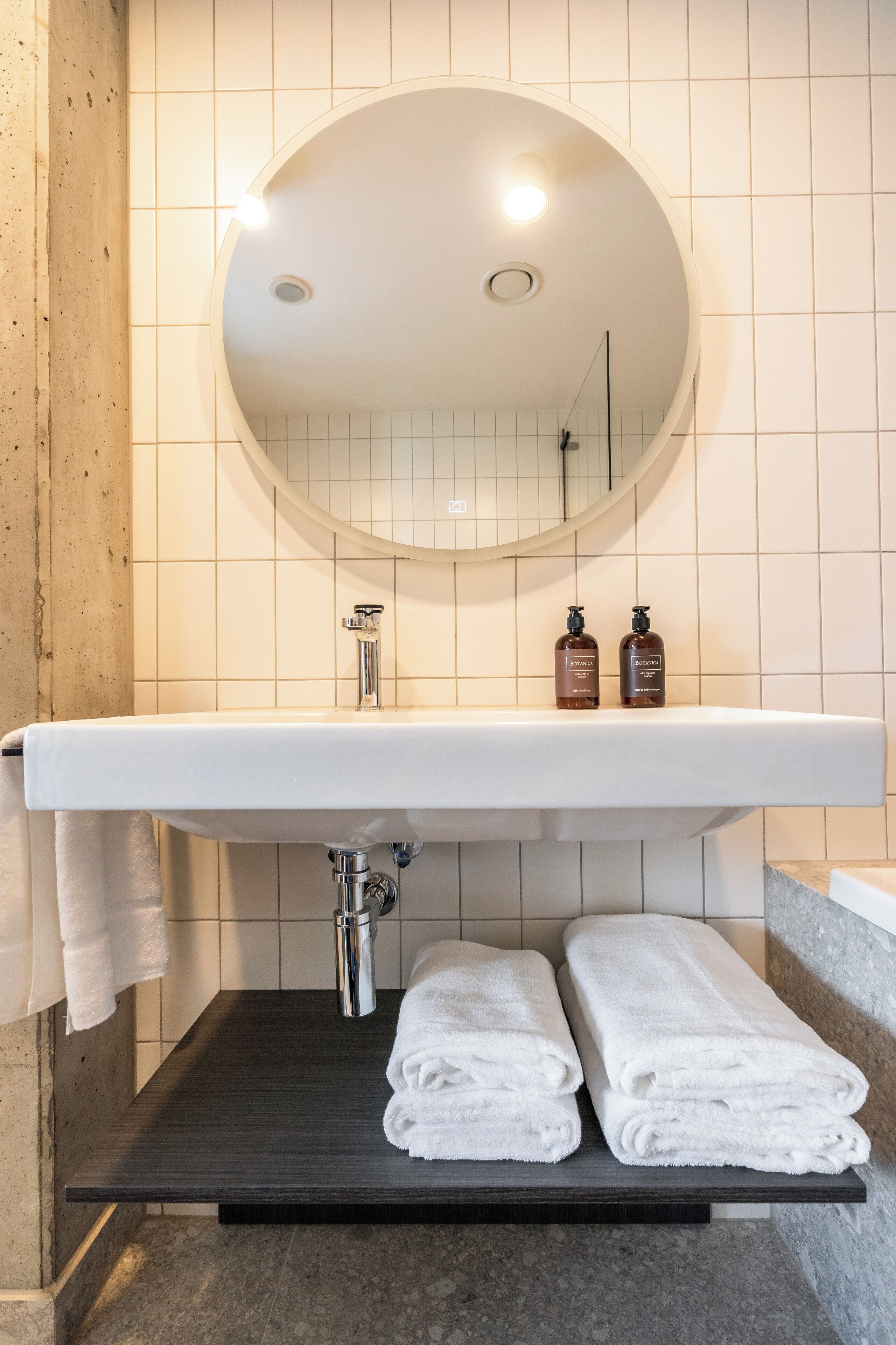 A bathroom with a white sink, a round mirror, and two bottles of shampoo.