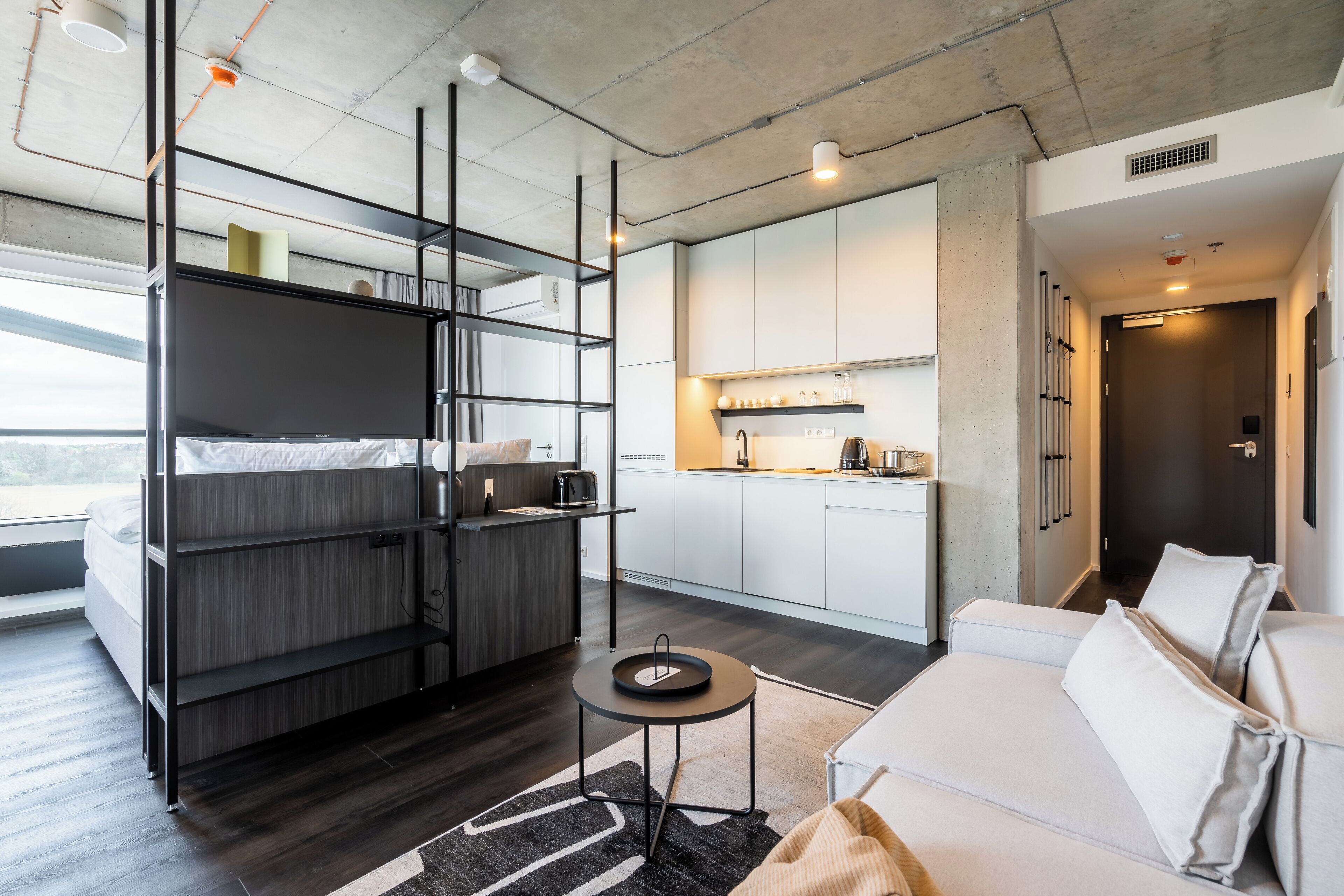 A modern, compact living space with a bunk bed, kitchenette, and a sofa.