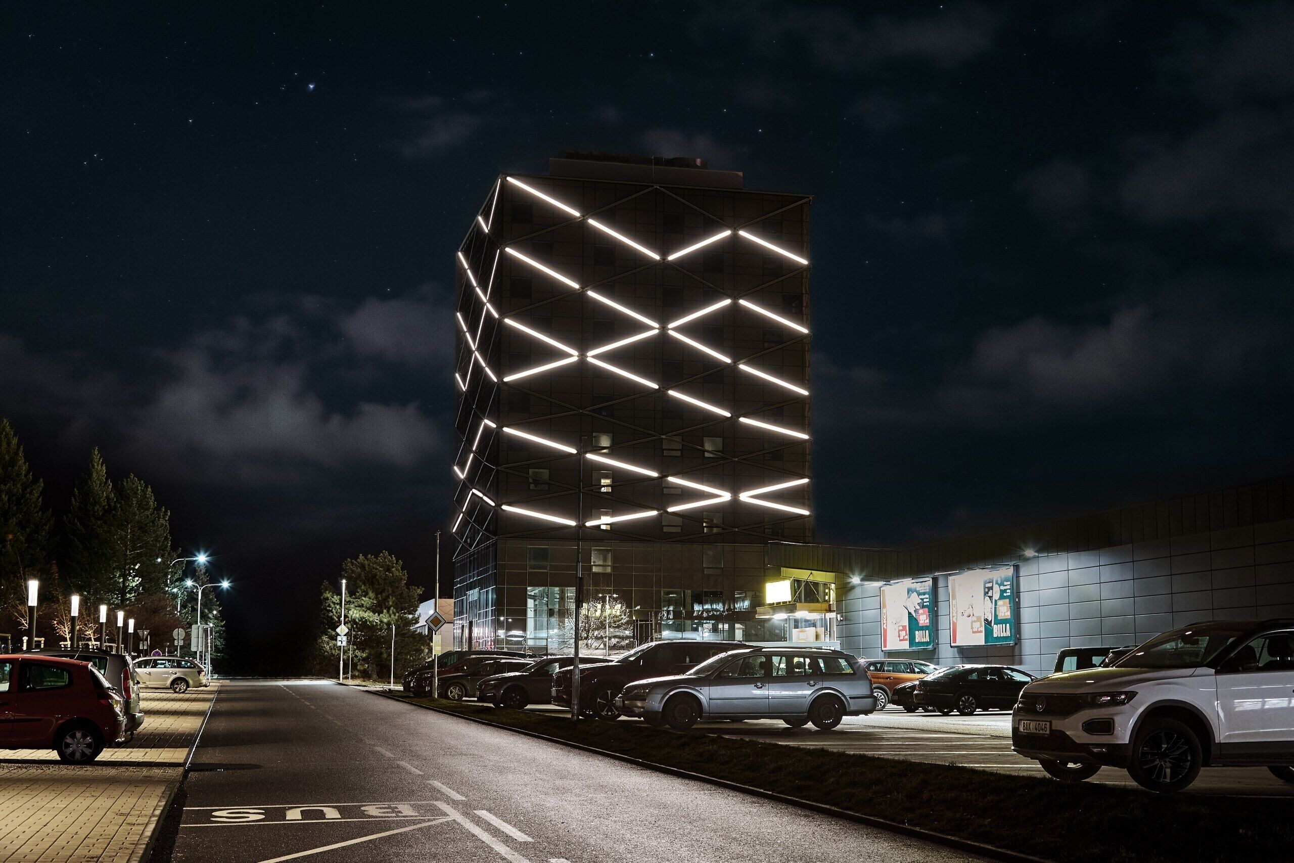 A modern building with a unique geometric facade and a parking lot with several cars.