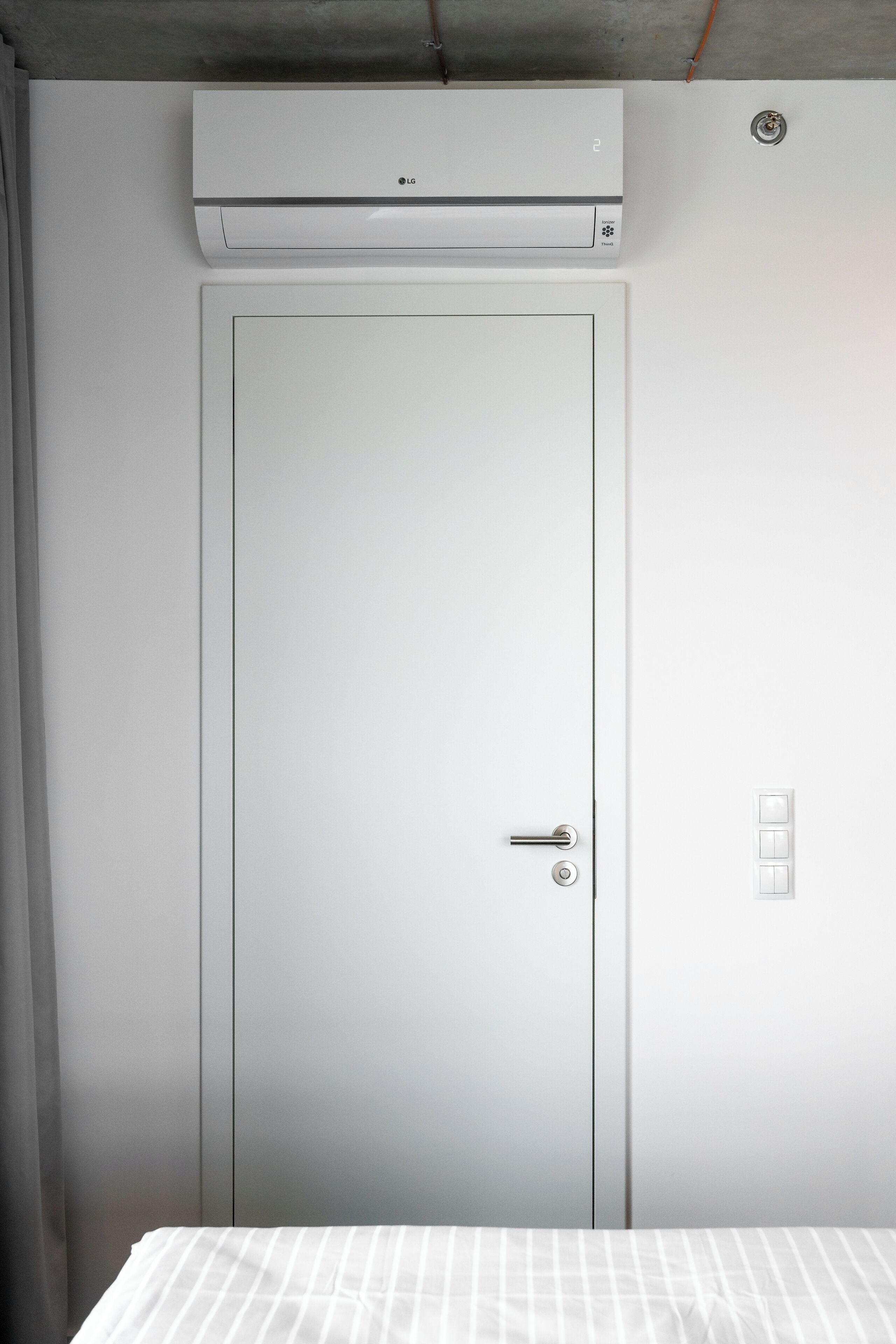 A white door with a keyhole and a handle, a white air conditioning unit above it, and a light switch to the right.