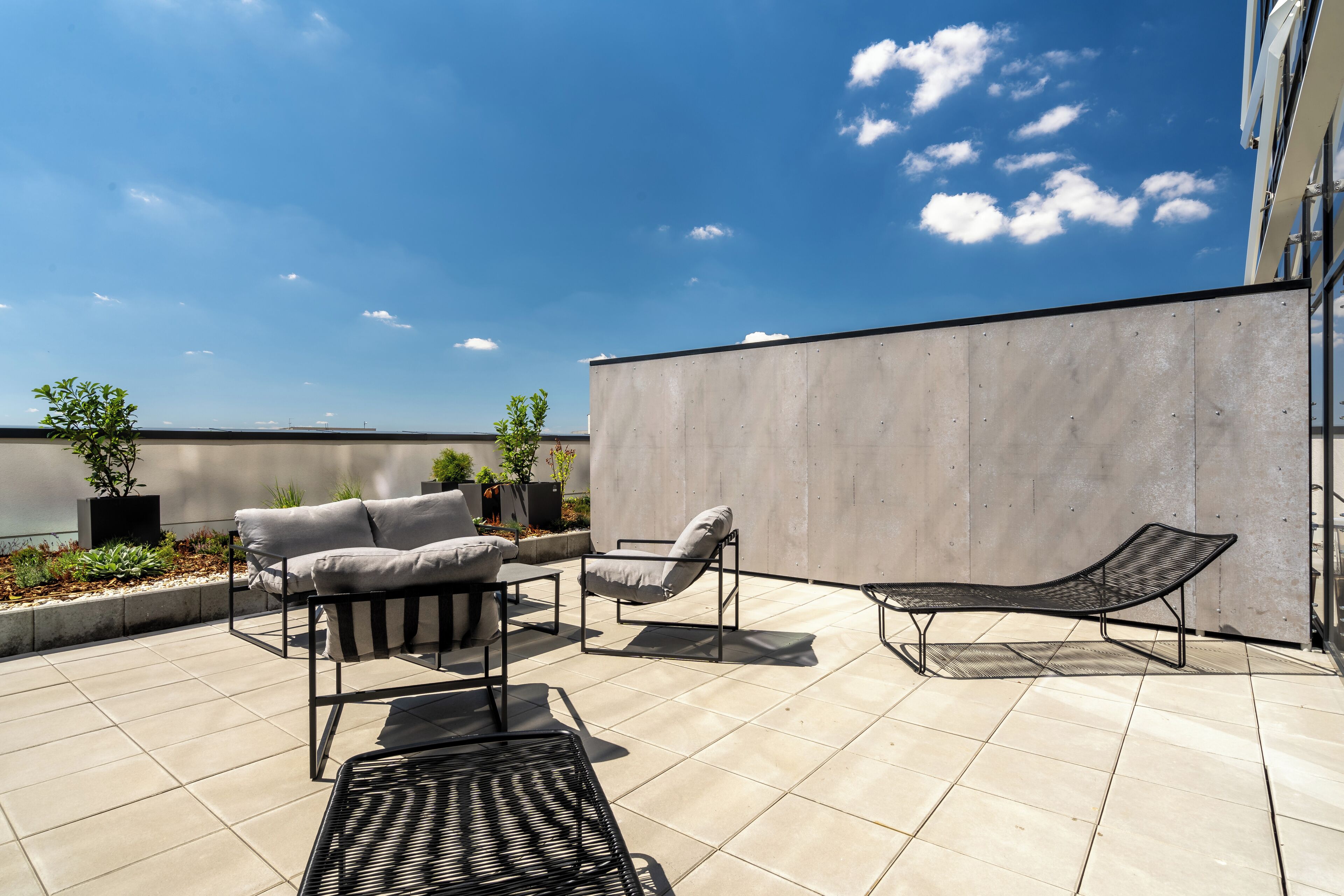 A rooftop patio with outdoor furniture, a view of the sky, and a concrete wall.