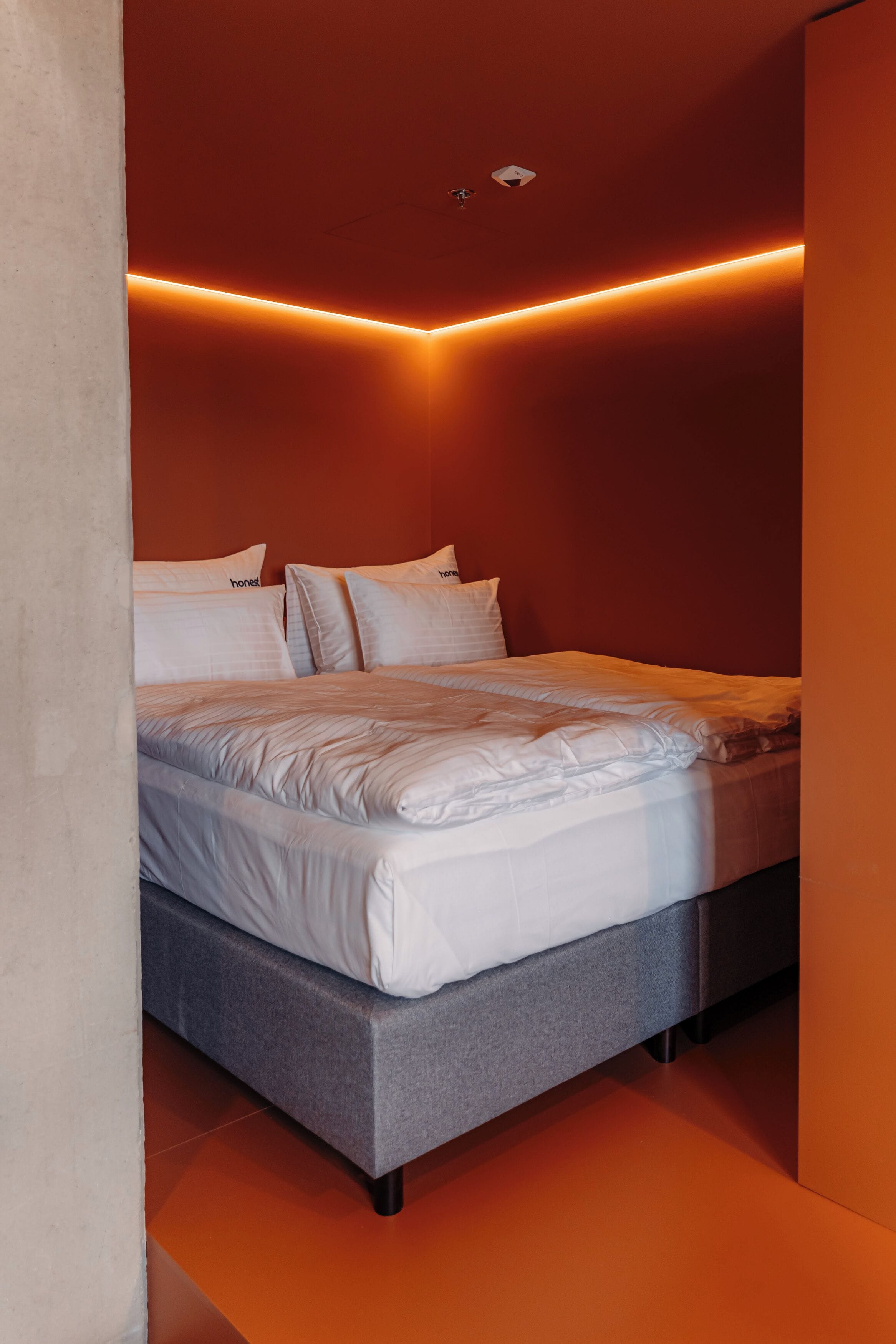 Ein modernes Schlafzimmer mit grauem Bett, weißer Bettwäsche und orangefarbenem Umgebungslicht.