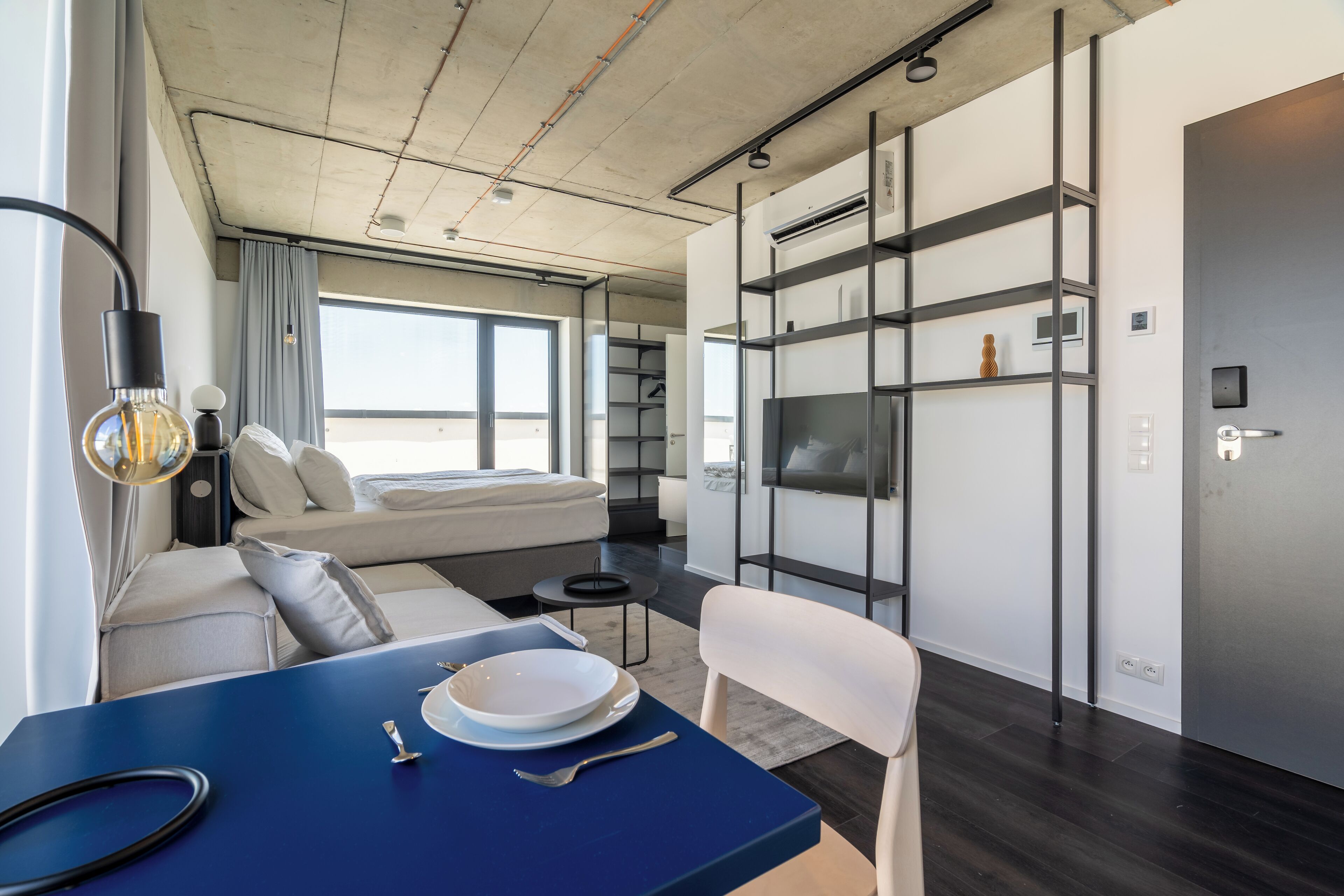 A modern, compact living space with a sofa, dining table, and built-in TV.