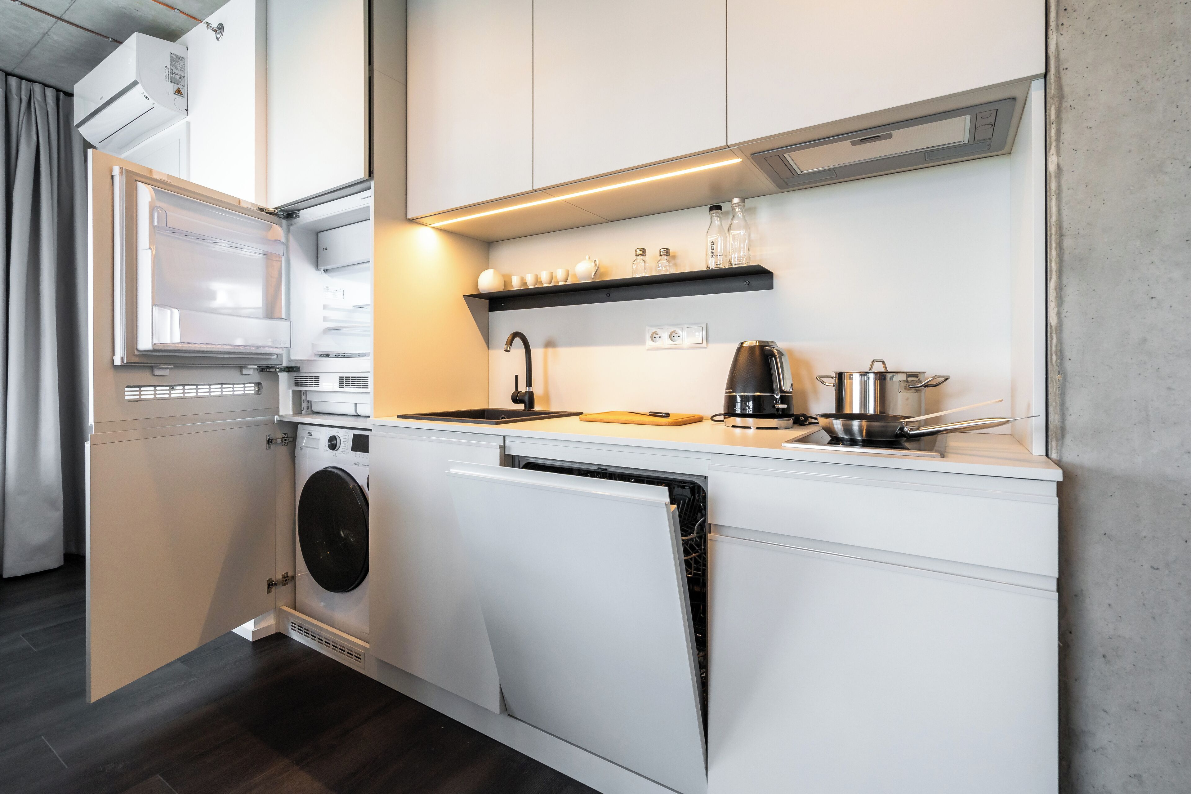 A compact kitchen with built-in appliances, a coffee maker, and a shelf with glassware.