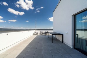 A rooftop terrace with a table and chairs, a view of the sky, and a wind turbine in the distance.