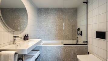 A modern bathroom with a large oval mirror, a white sink, a bathtub, and a toilet.