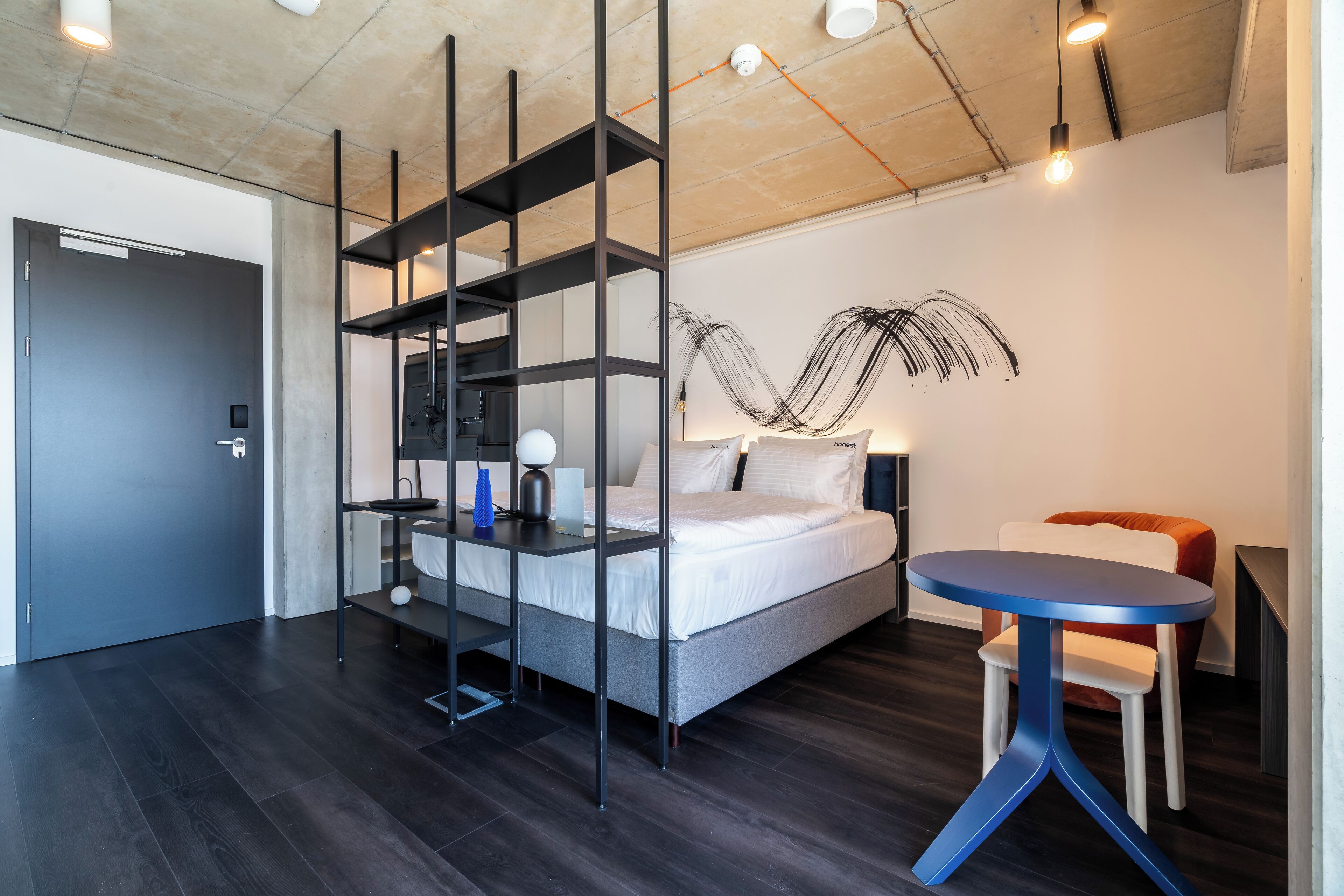 A modern hotel room with a bed, a round table, and a unique wall art piece.