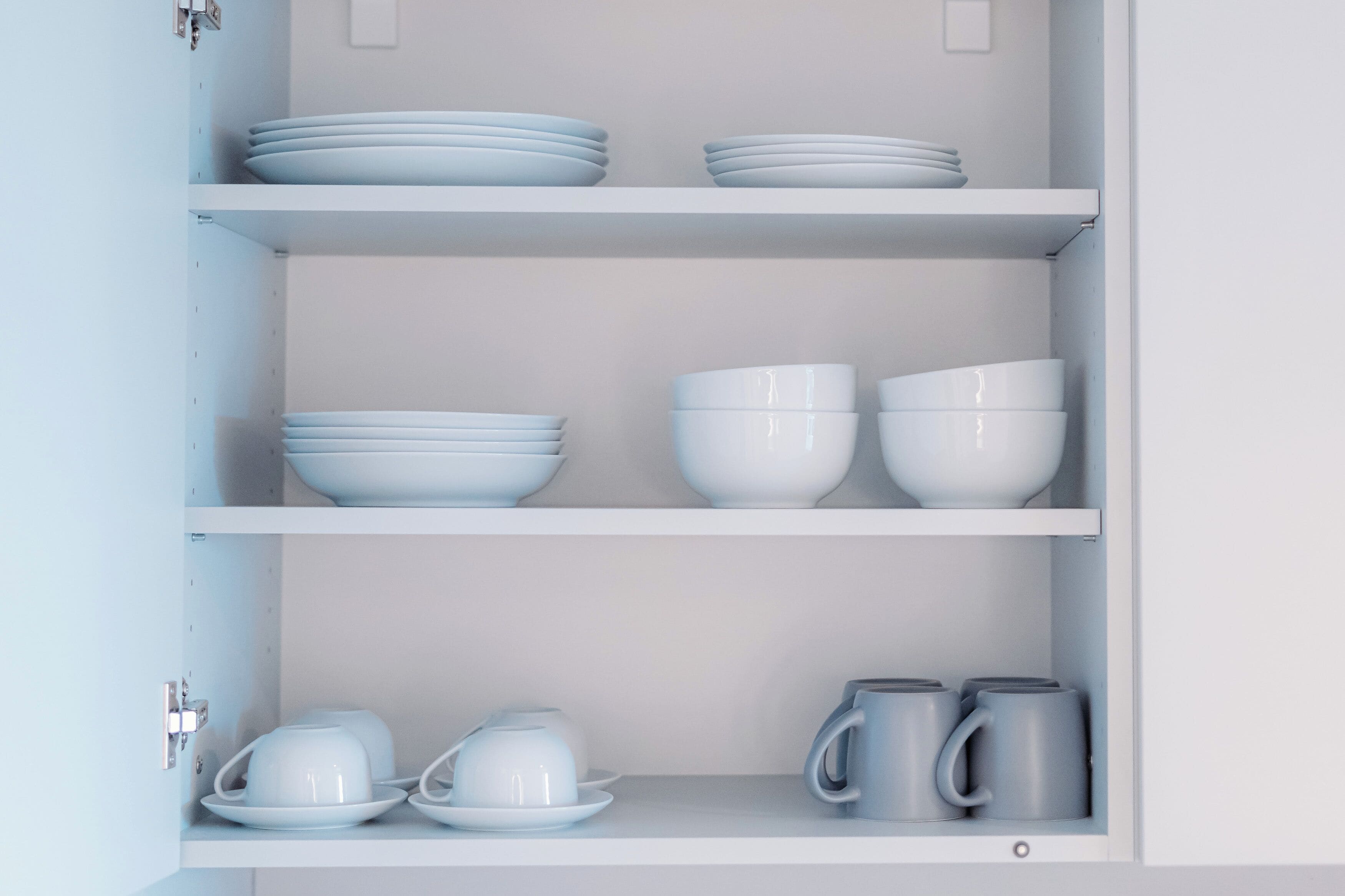A white cabinet with shelves containing white bowls, plates, and grey mugs.