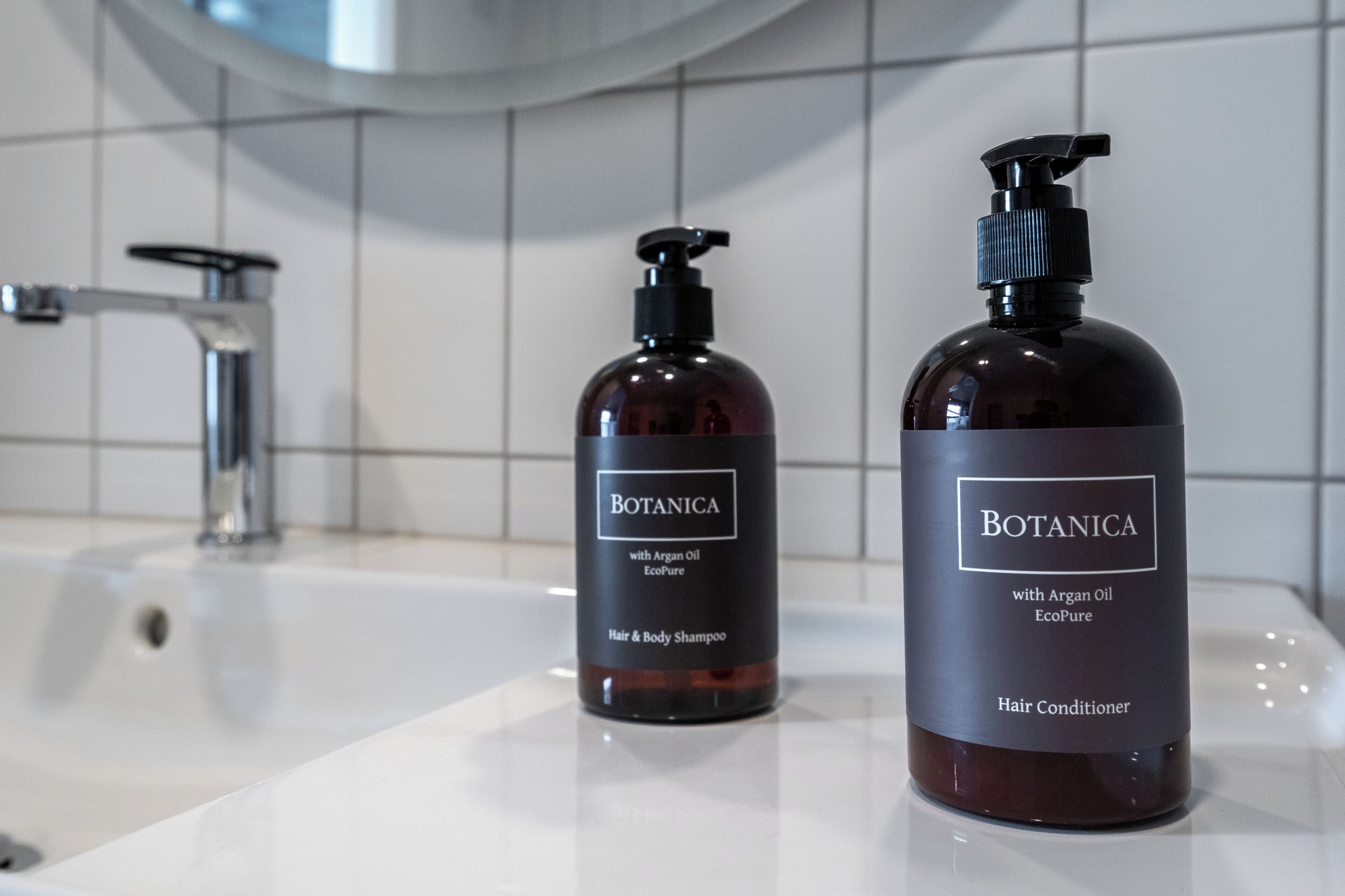 Two bottles of Botanica hair and body shampoo and conditioner on a bathroom sink.