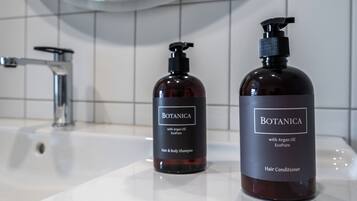 Two bottles of Botanica hair and body shampoo and conditioner on a bathroom sink.