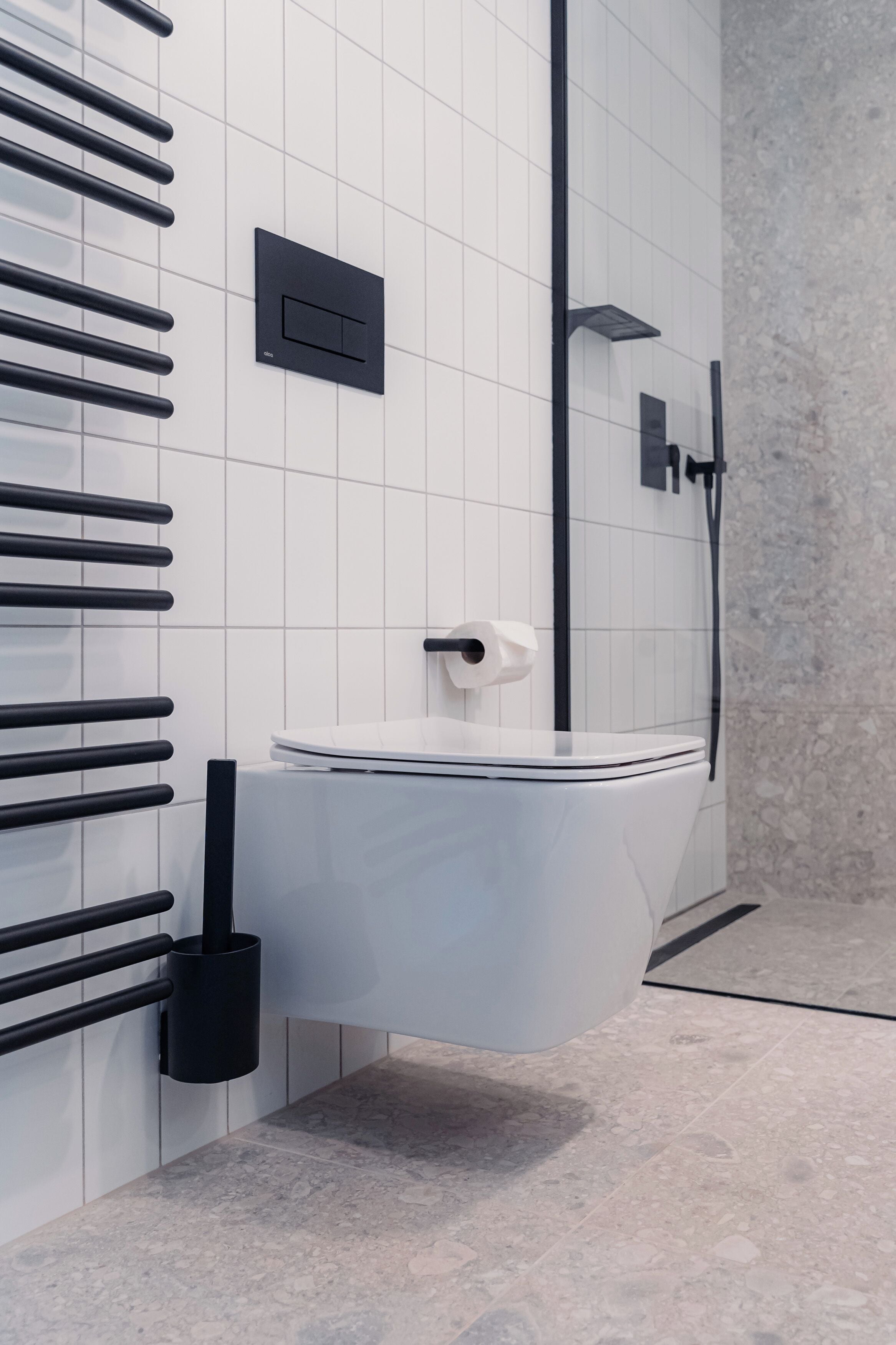 A modern bathroom with a white toilet, black towel racks, a black soap dispenser, and a showerhead.