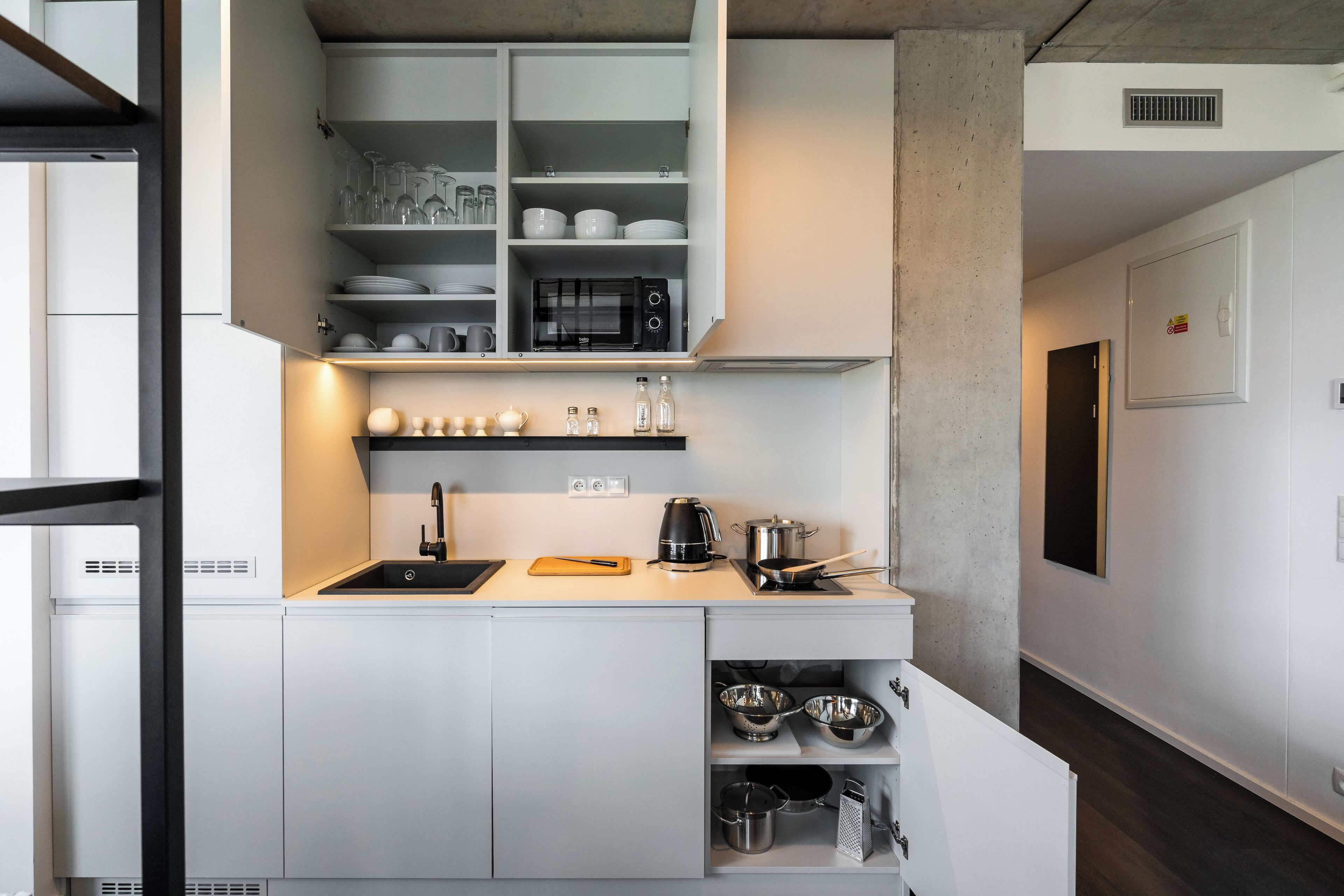 Una cocina moderna con armarios blancos, microondas integrado y cafetera.
