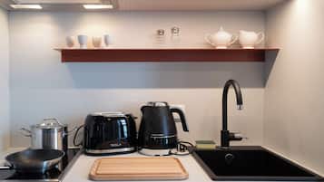 Een kleine keuken met een kookplaat, een koffiezetapparaat, een waterkoker, een spoelbak en een houten snijplank.