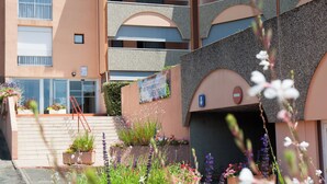 A multi-story building with a modern design, featuring balconies and a central entrance with steps.