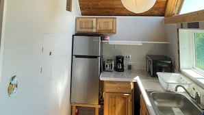 A compact kitchen with wooden cabinets, a refrigerator, a toaster, a coffee maker, and a sink. - Cozy Cottage (Surry)
