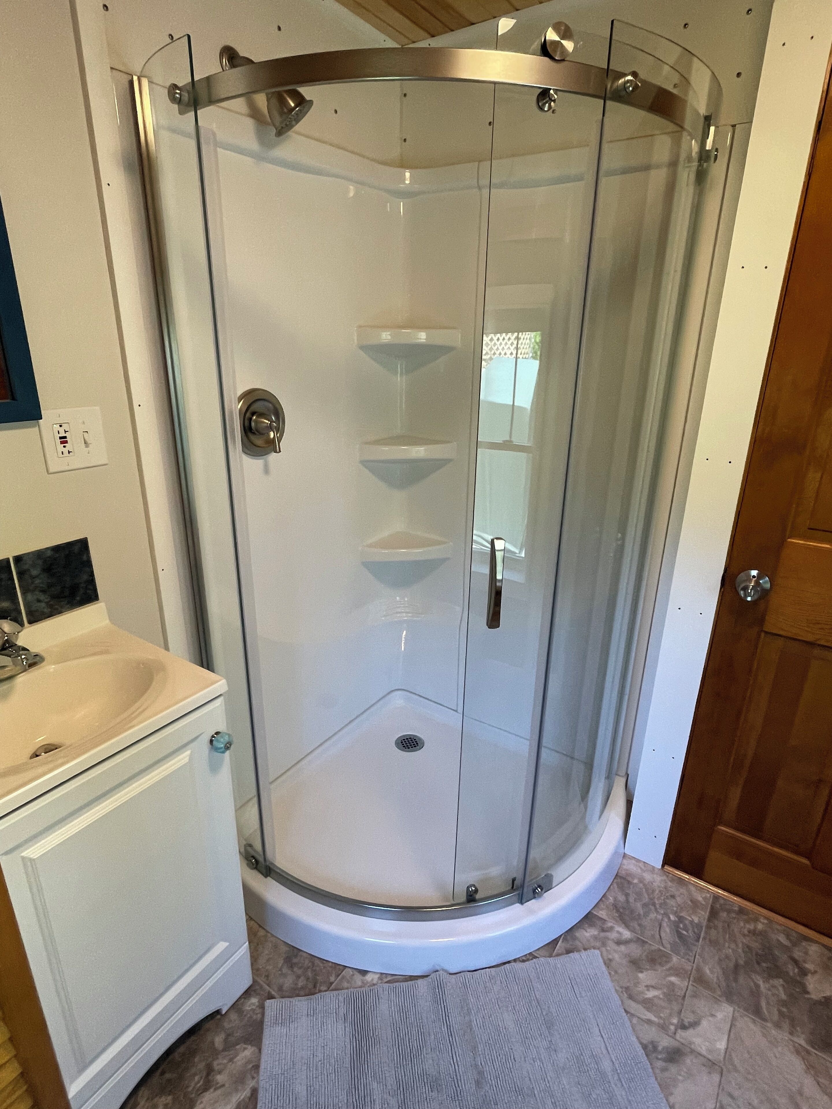A glass-enclosed shower stall with a white sink and vanity to the left.