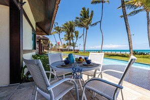A poolside dining area with white wicker chairs and a table set for two, overlooking a pool and the ocean. - Bangalô 4qts BeiraMar em Muro Alto-SH034 (Ipojuca)