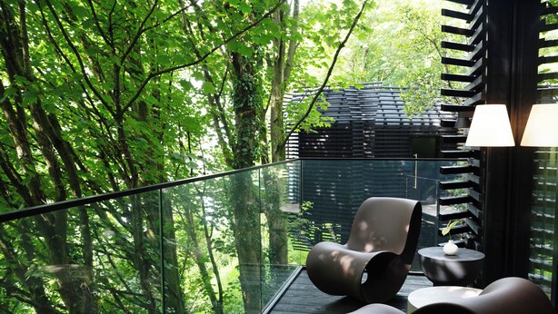 Un espace extérieur moderne, aménagé avec des sièges et doté d’une balustrade en verre donnant sur une zone boisée.