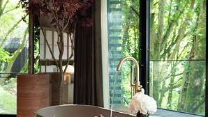 Une salle de bain moderne avec une grande baignoire, une plante en pot et une vue sur une forêt, visible à travers de grandes fenêtres.