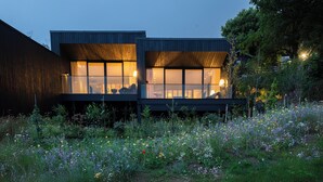 Une maison moderne à deux étages, dotée de grandes fenêtres et d’un jardin où poussent différentes sortes de fleurs.