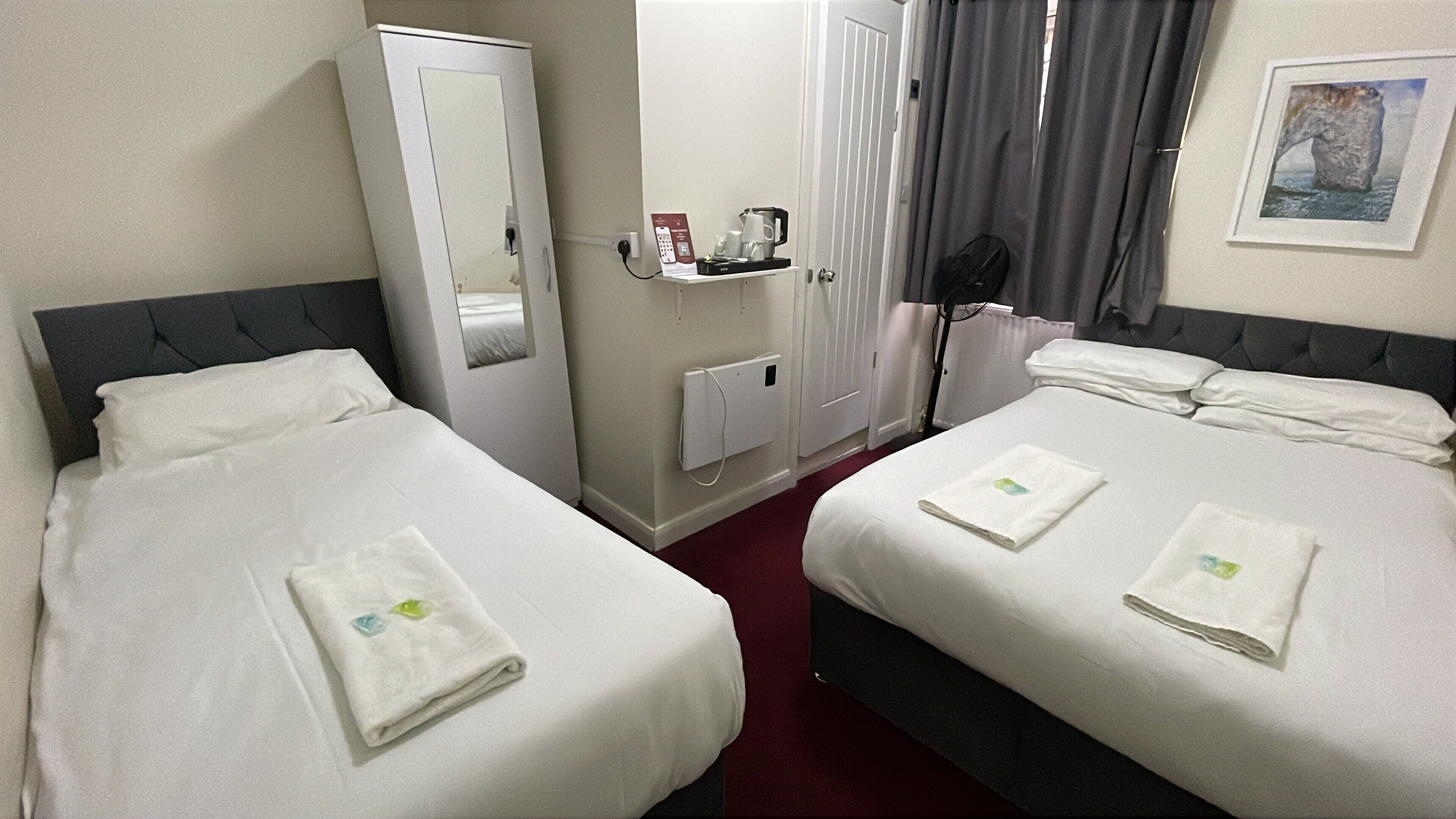 A hotel room with two beds, a wardrobe, a mirror, a coffee maker, and a framed picture on the wall.
