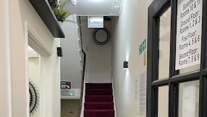 A hotel corridor with a red carpet, a staircase, and signs indicating room numbers and floors. - Oban Victoria Hotel (London)